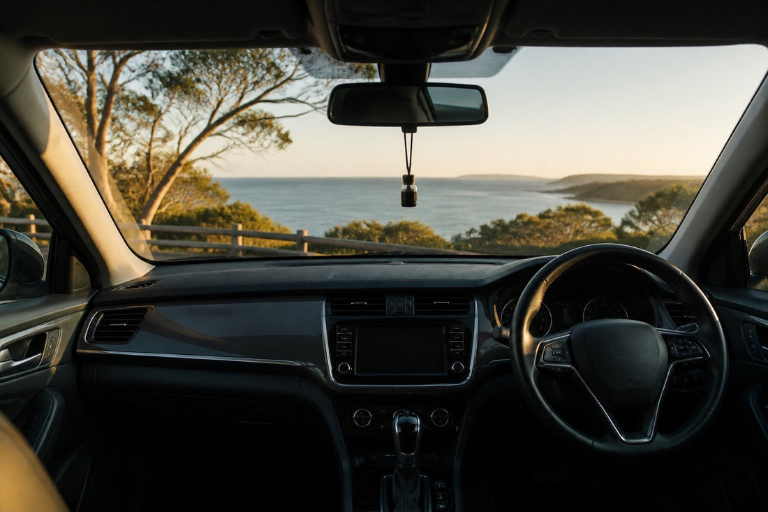 Right-hand-drive car interior overlooking an Australian coast at golden hour with a small hanging fragrance diffuser