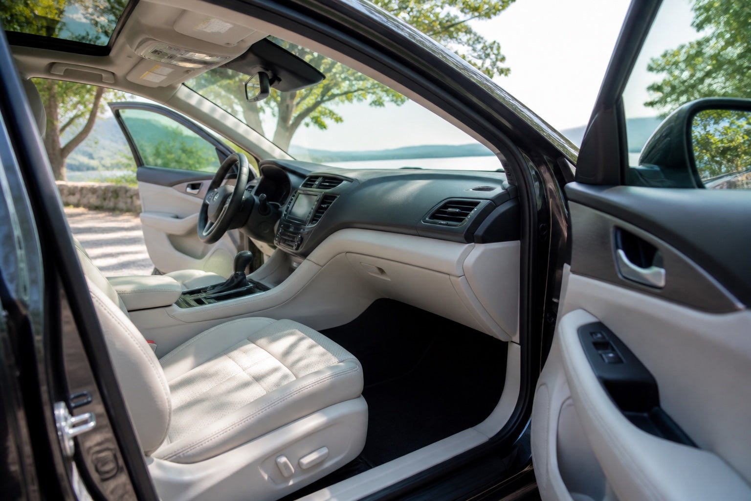 Clean modern car interior with both front doors open to fresh air at a leafy lookout
