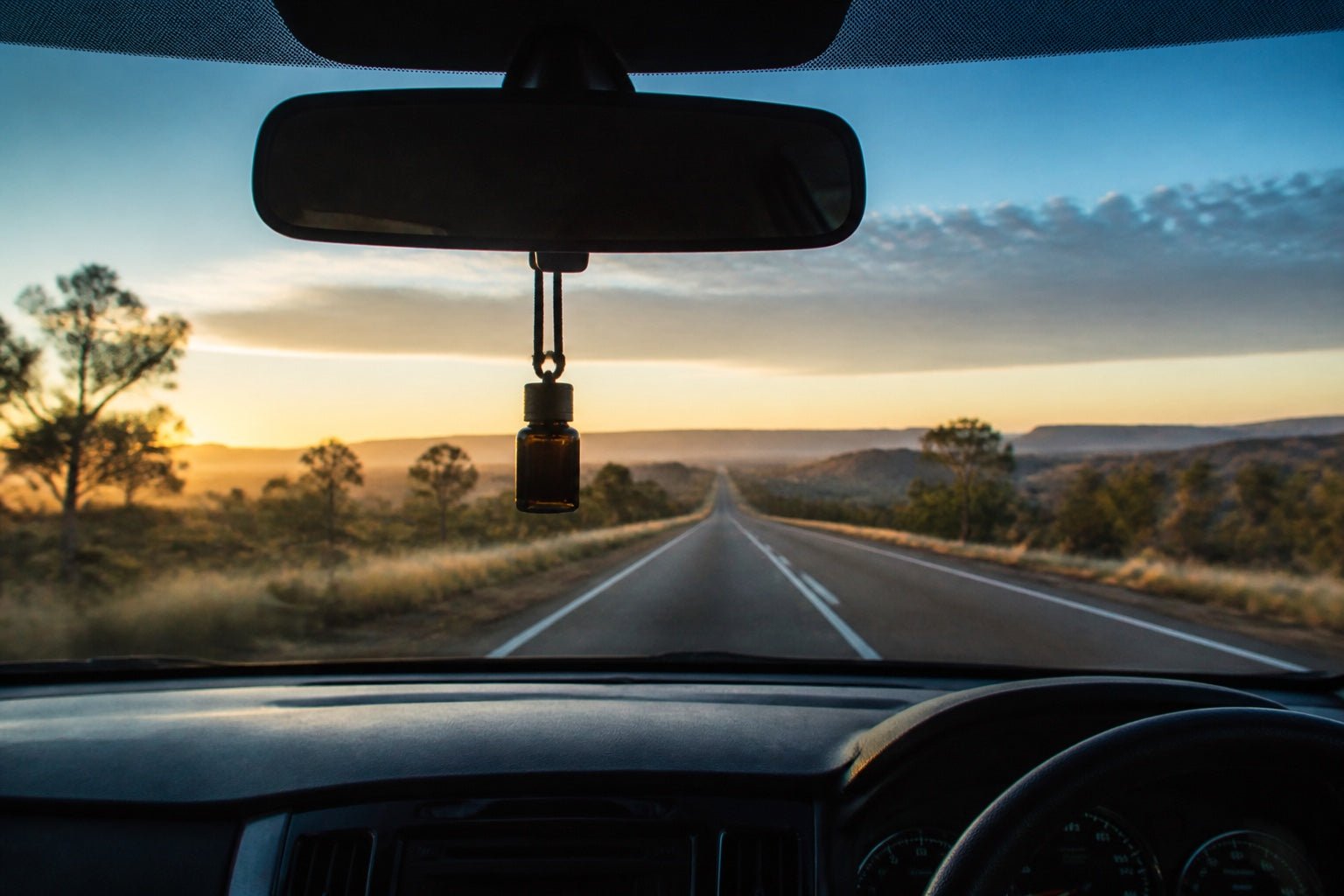 Small hanging car diffuser silhouetted against a long Australian country road at sunrise