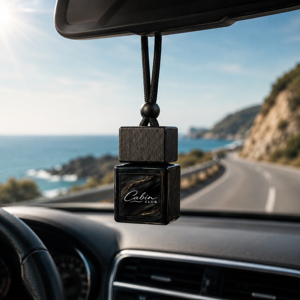 Cabin Club Coastal Drive car fragrance diffuser hanging from a rear-view mirror on a sunlit coastal road